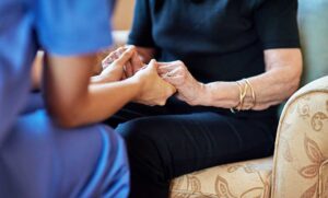 A social worker talking with a senior resident and family member at a table in a comfortable assisted living common room.