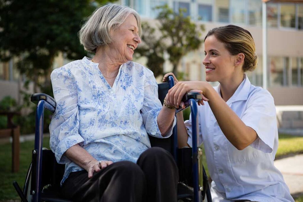 Older adults chatting and walking together along a garden path in an assisted living community.