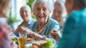 Caregiver reviewing a medication chart beside an older resident at a dining table with labeled pill containers.